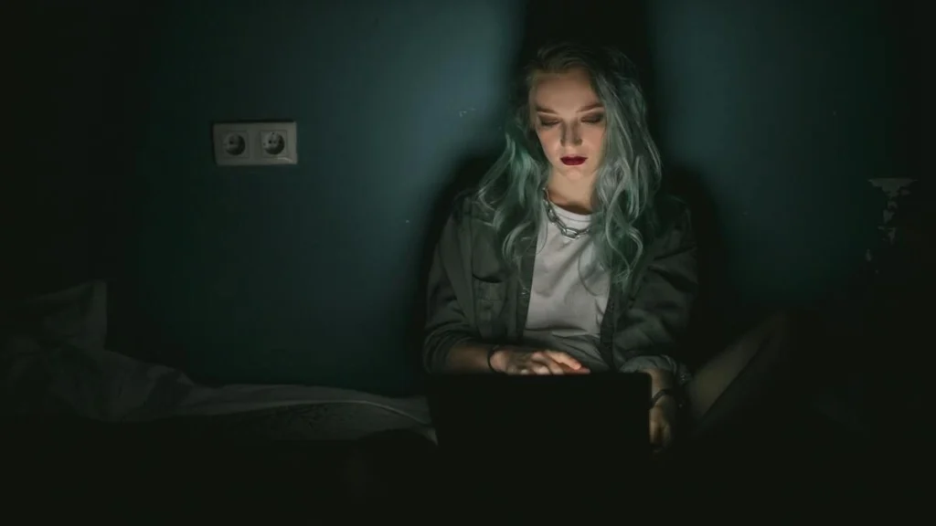 暗い寝室で女性がパソコンを操作している画像