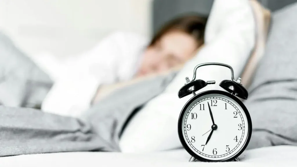 ベッドサイドの目覚まし時計と女性が寝ている画像